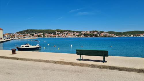 a bench sitting next to a body of water with a boat at Apartments Valentina Tisno in Tisno