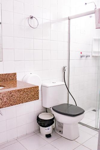 a white bathroom with a toilet with a black seat at Hotel Primavera Betim in Betim