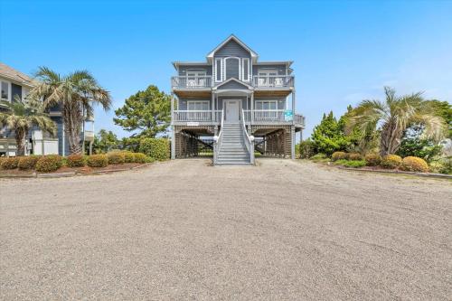 a large house on a gravel driveway with palm trees at Prime Time in Caswell Beach