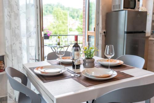 a table with plates and wine glasses and a refrigerator at Appartamento Rayan Alba Wine Retreat nelle Langhe in Alba