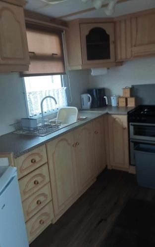 a kitchen with wooden cabinets and a sink and a stove at Highfield and the Haven Caravan Skegness in Lincolnshire