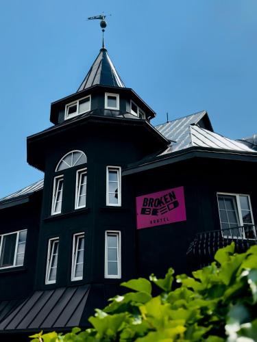 a black building with a tower with a pink sign on it at Broken bed hootel in Kaunas