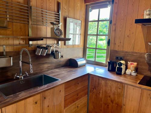 a kitchen with wooden cabinets and a sink and a window at Paisible cottage au bord de l'eau -15 mn des côtes in Pierrefitte-en-Auge