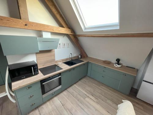 Elle comprend une petite cuisine avec des placards bleus et une fenêtre. dans l'établissement le gite de la pommeraie, à Le Bois-Robert