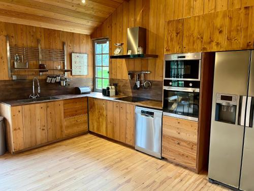 a large kitchen with wooden cabinets and stainless steel appliances at Paisible cottage au bord de l'eau -15 mn des côtes in Pierrefitte-en-Auge