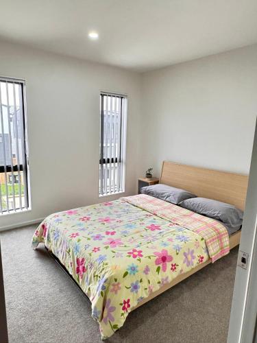 a bedroom with a bed with a floral comforter and two windows at 3BR Auckland Holiday Home near Outlet shops and Costco in Auckland