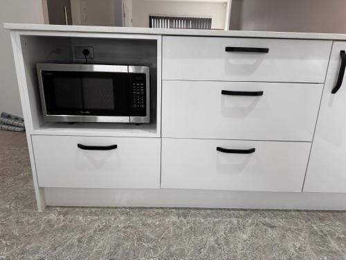 a white cabinet with a microwave on top of it at 3BR Auckland Holiday Home near Outlet shops and Costco in Auckland