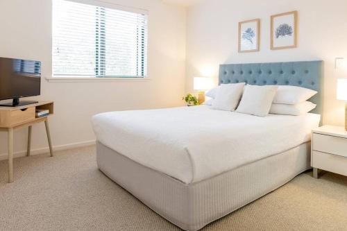 a white bedroom with a large bed and a television at Charming Riverside Noosa gem in Noosaville