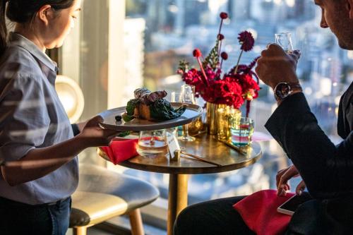 a woman sitting at a table with a plate of food at voco Auckland City Centre by IHG in Auckland