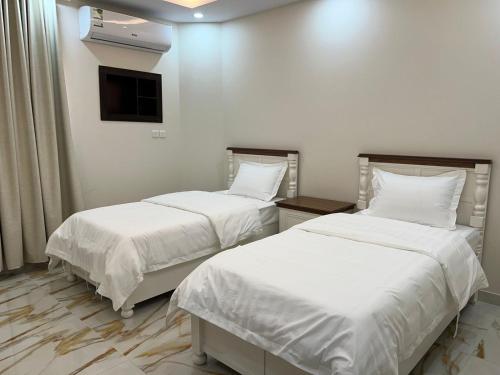 a room with two beds with white sheets and a tv at شقق سطام المخدومة in Al Fayşalīyah
