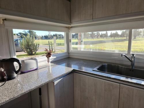 une cuisine avec un évier et deux fenêtres dans l'établissement Casa en Club de Campo. Parque y Pileta., à San Nicolás de los Arroyos
