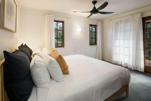 a bedroom with a white bed with pillows and a ceiling fan at Grove Hinterland Retreat - 15 mins to beach in Kiels Mountain