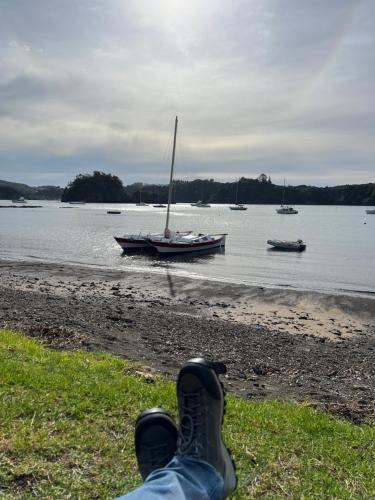 a person laying on the beach with a sail boat in the water at Tutukaka Sunrise in Tutukaka