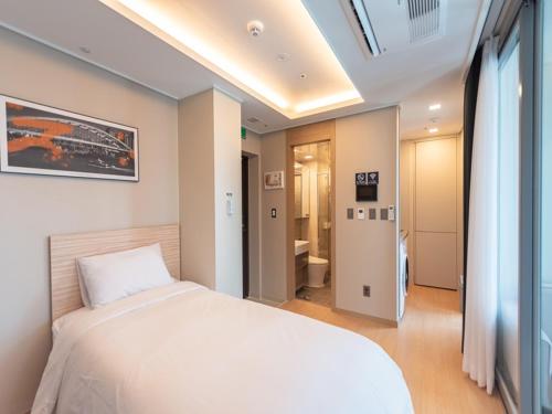 a bedroom with a white bed and a bathroom at Elmomento Haeundae in Busan