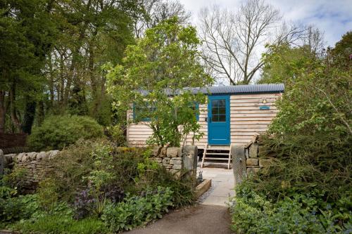 a tiny house with a blue door in a garden at Mr McGregor’s Garden Shepherds Hut Chatsworth Estate in Baslow