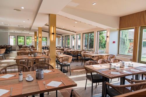 ein Restaurant mit Holztischen, Stühlen und Fenstern in der Unterkunft Hotel Karos Spa in Zalakaros
