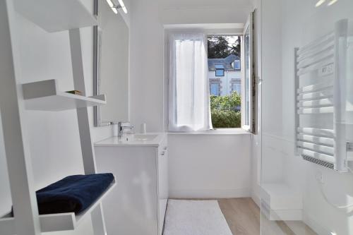 une salle de bain blanche avec un lavabo et une fenêtre dans l'établissement Les Myosotis du Val - Duplex à quelques pas de la mer, à Pléneuf-Val-André