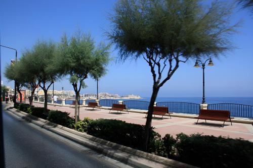 a row of benches on a sidewalk near the water at Manoel De Vilhena Holiday Apartments in Il-Gżira