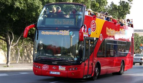a red double decker bus driving down a street at Manoel De Vilhena Holiday Apartments in Il-Gżira