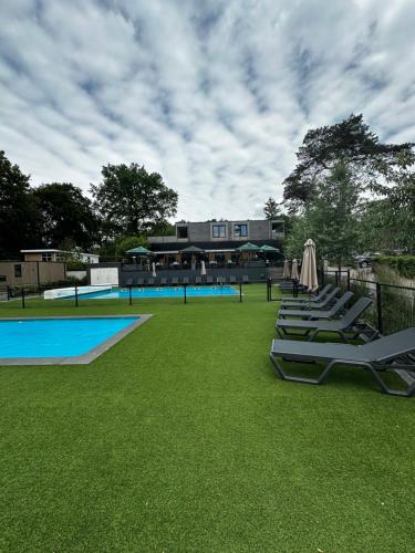 a group of lounge chairs sitting on the grass near a pool at Dubbele chalet op recreatiepark Topparken op de Veluwe in Beekbergen met grote vrije tuin en eigen parkeerplaats in Beekbergen