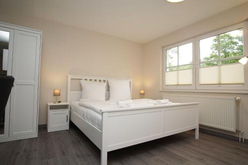 ein weißes Schlafzimmer mit einem weißen Bett und zwei Fenstern in der Unterkunft Ferienhaus Inselhus Haus - Terrasse, Garten in Glowe