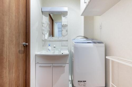 a small white bathroom with a sink and a refrigerator at Komachi Hotel Nipponbashi in Osaka