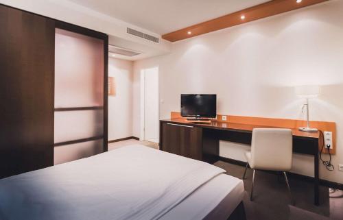 a bedroom with a bed and a desk with a television at elaya hotel stuttgart ludwigsburg ehemals Abacco by Rilano in Korntal-Münchingen