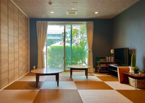 a living room with two tables and a large window at HOSTEL SunTerrace Ishigaki in Ishigaki Island
