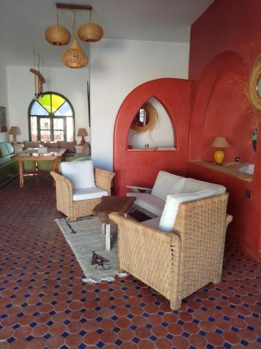a living room with wicker chairs and a red wall at Villa Nouran - Chambre Hôte in Ghazoua