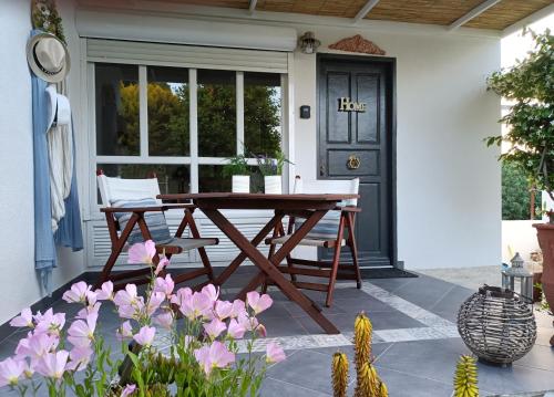 una mesa de madera y sillas en un porche con flores rosas en Casa Martina 2 (Spata) 10min El.Venizelos airport. en Spáta