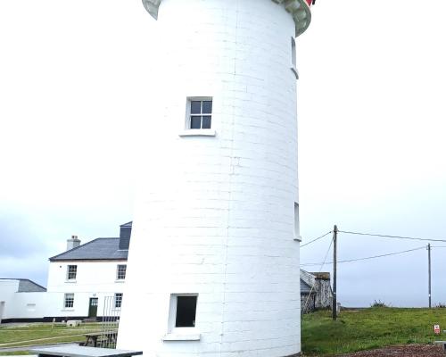 a white lighthouse in front of a white house at Loop Head Lighthouse Attendant's Cottage in Kilbaha