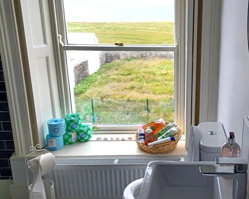 a bathroom window with a sink and a basket of toiletries at Loop Head Lighthouse Attendant's Cottage in Kilbaha
