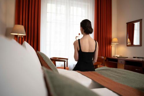una mujer parada en una habitación de hotel mirando por la ventana en Spa & Wellness Hotel Olympia Marienbad, en Mariánské Lázně