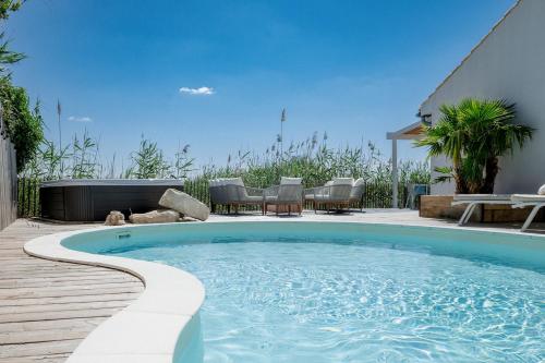a swimming pool with chairs and a table on a patio at La Perle Rose Villa Standing 5 étoiles avec piscine jacuzzi et superbe vue in Aigues-Mortes