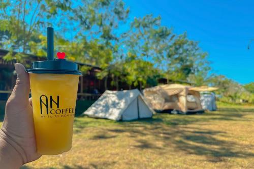 a hand holding a cup of coffee in front of a tent at An Homestay in Di Linh