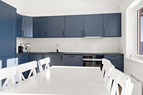 a kitchen with blue cabinets and a white table and chairs at Voss Resort self-service apartments in Skulestadmo