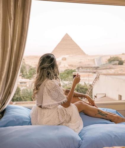 a girl sitting on a bed taking a picture of the pyramids at Royal Crown Hotel Giza Pyramids View in Cairo