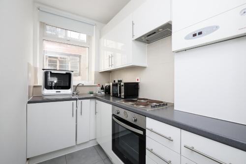 a white kitchen with white cabinets and a microwave at Stylish Fitzrovia Studios W1 in London