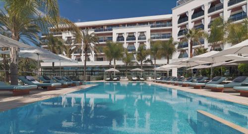 a swimming pool with chairs and umbrellas in front of a building at Aguas de Ibiza Grand Luxe Hotel - Small Luxury Hotel of the World in Santa Eularia des Riu