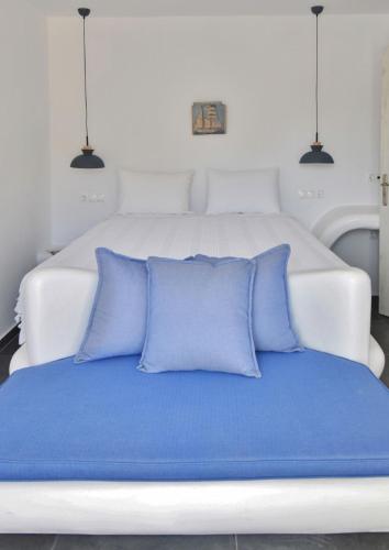 a white bed with blue pillows on it at Tinos Portraits Ballos in Agios Romanos