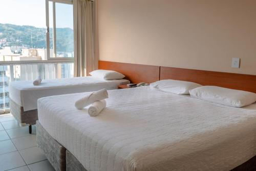 two beds in a hotel room with a large window at Rede Andrade Cecomtur in Florianópolis