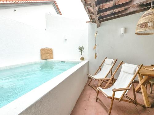 a swimming pool with two chairs and a table at Costa Inn Beach House with Pool by Homeful Homes in Costa da Caparica