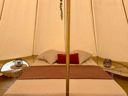 a bed in a tent with a red pillow on it at Chambre au jardin Tente de charme in Éguzon-Chantôme