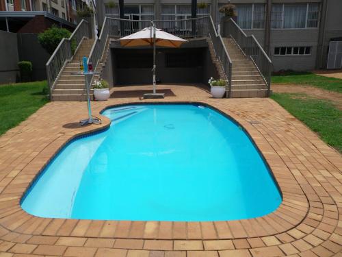 a large blue swimming pool with an umbrella and stairs at Apollo Hotel in Johannesburg