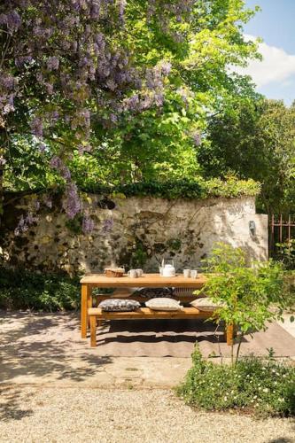 a wooden table under a tree with purple flowers at Gîte Glycine pour 8 personnes avec sauna et bain nordique in Capian