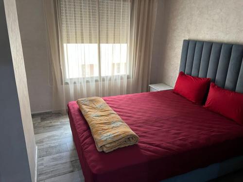 a bedroom with a red bed with red pillows and a window at Appartement Cosy Available in Kenitra