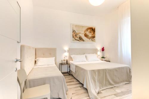 a white bedroom with two beds and a chair at Residence Diffuso Arcobaleno in Gabicce Mare
