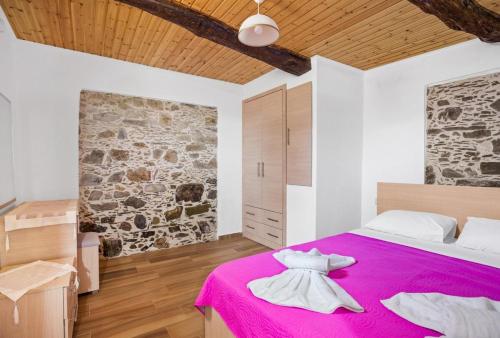 a bedroom with a pink bed with a stone wall at Maria's House with View in Kambos in Kámbos