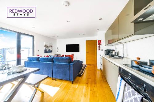 a kitchen and living room with a blue couch at PENTHOUSE SERVICED APARTMENT IN CAMBERLEY TOWN CENTRE, WITH FREE PARKING, FREE WiFi, LIFT AND BALCONY ACCESS, PERFECT FOR BUSINESS STAYS, FAMILIES, RELOCATIONS, EXTENDED STAYS, AND EMERGENCY ACCOMMODATION by REDWOOD STAYS in Camberley