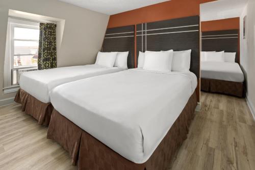 two beds in a hotel room with white sheets at Wildwood Inn Hotel Travelodge Beach & Boardwalk in Wildwood